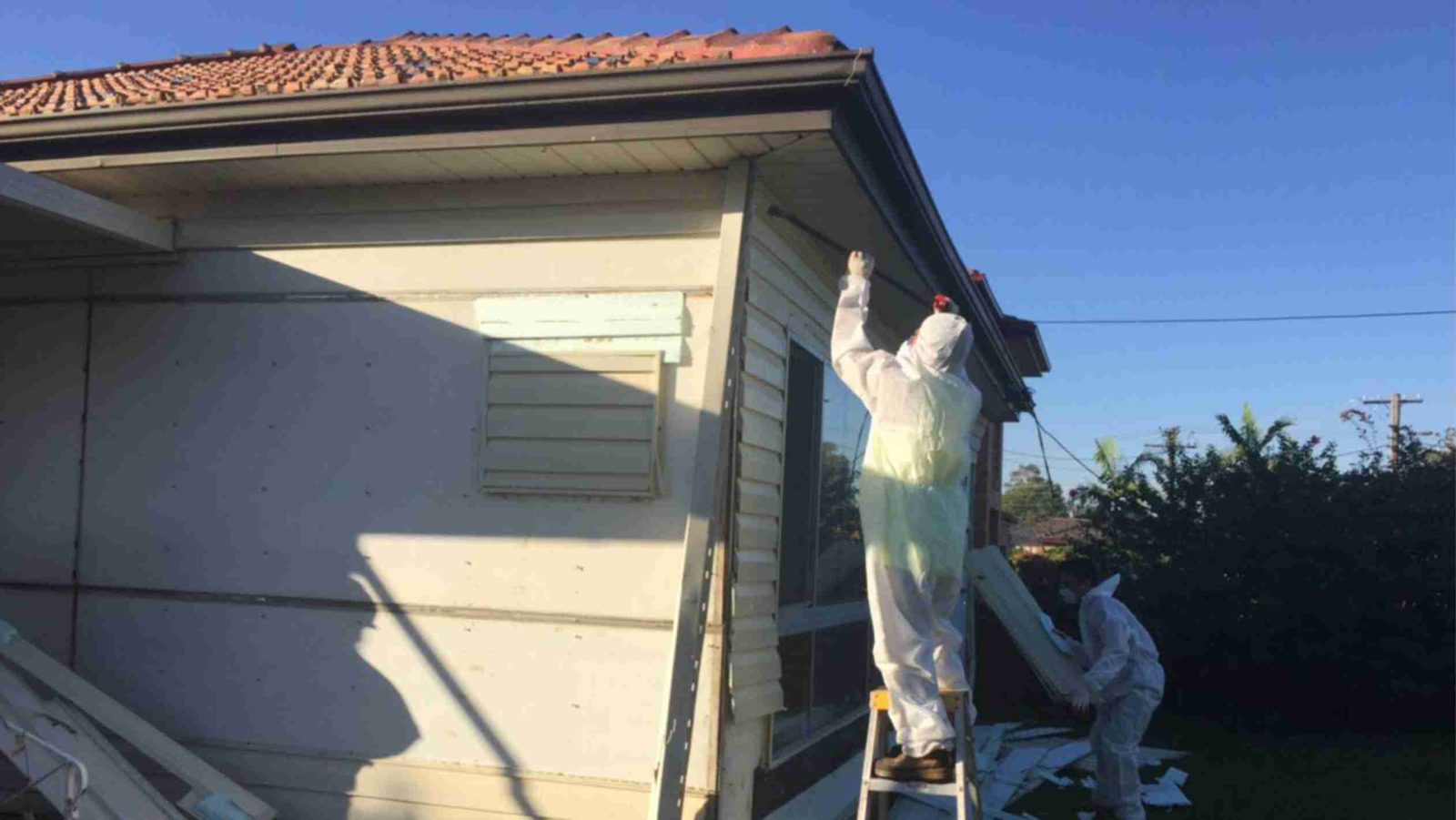A worker in a protective suit removing old sheeting from the outside of a house