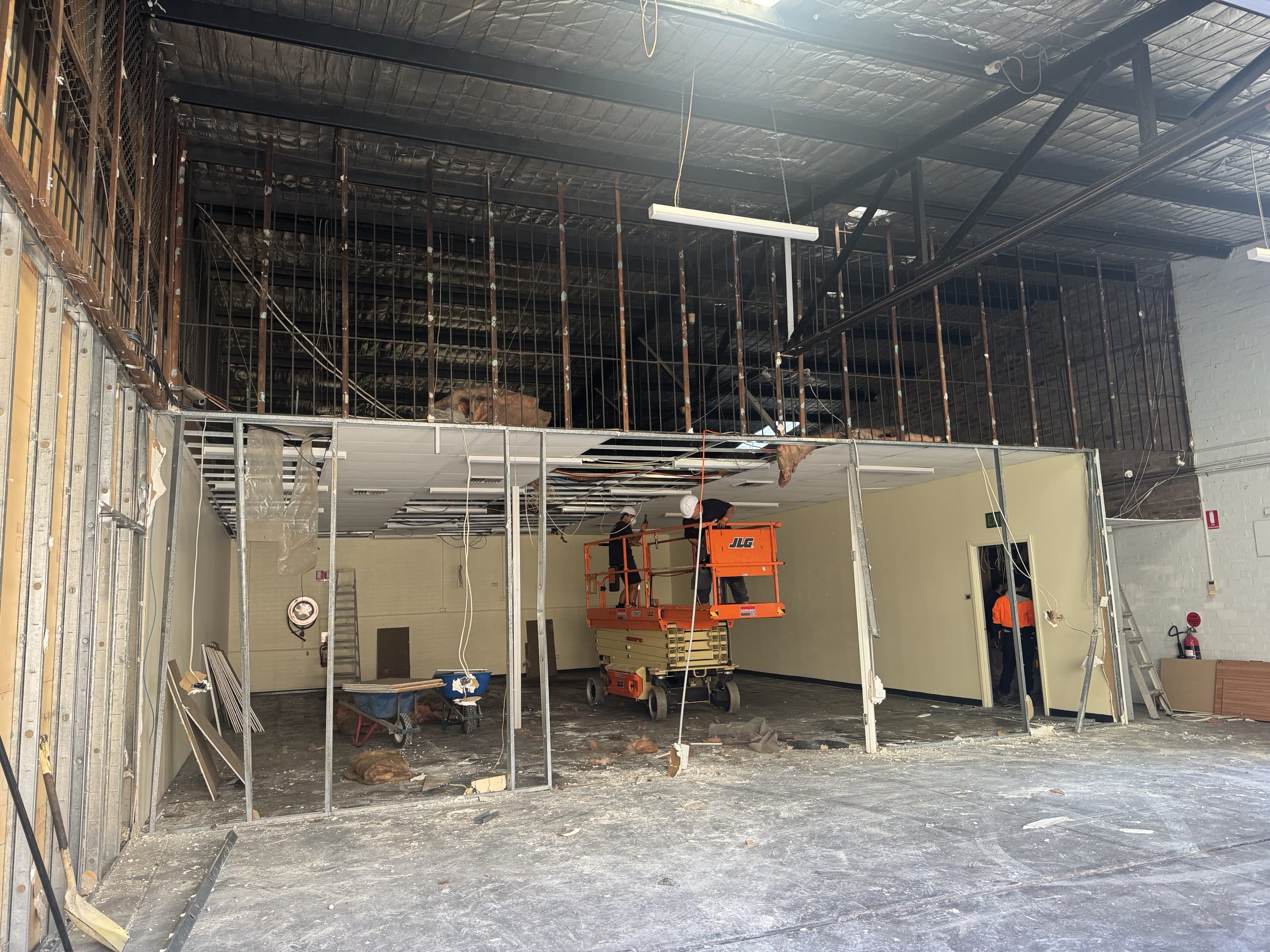 Two construction workers on a scissor lift repair a ceiling inside a gutted commercial building.